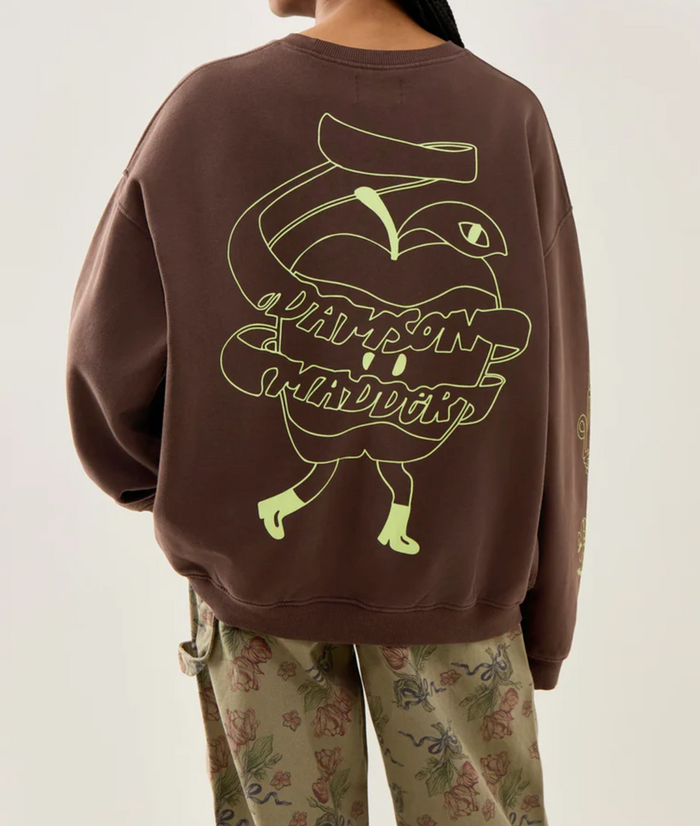 Person wearing a brown sweatshirt with a green graphic design on the back, standing against a plain background.