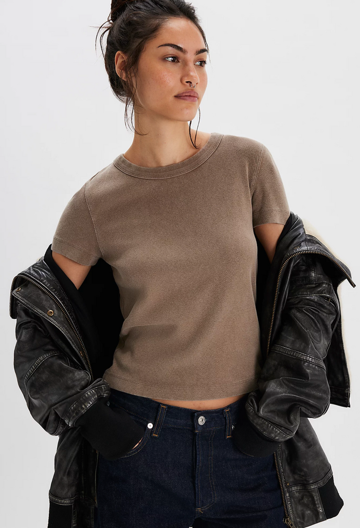 Woman wearing a cocoa Free People t-shirt and black leather jacket on a white background