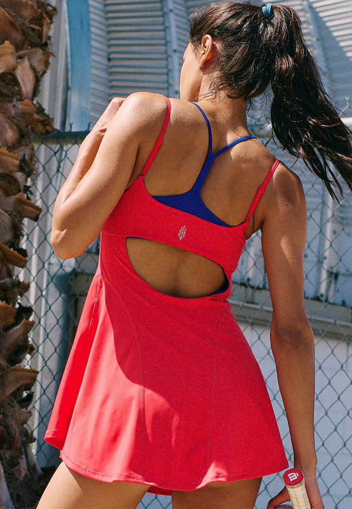 Woman in a grapefruit dress with blue bra top standing outdoors against a chain-link fence.