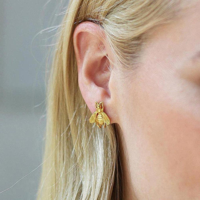 Gold bee stud earrings in a woman's ear.