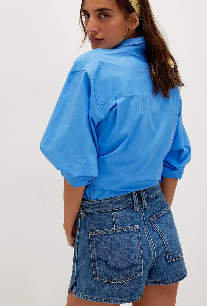 Back view of person wearing a blue shirt and denim shorts on a white background