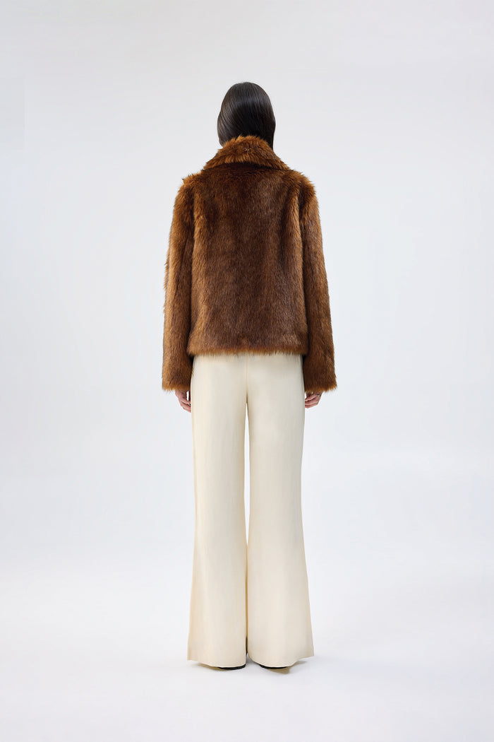 Rust brown faux fur jacket with notch lapel and cropped fit, worn over cream wide-leg trousers, back view