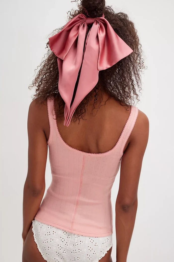 Person wearing a pink tank top with a bow on the head against a white background