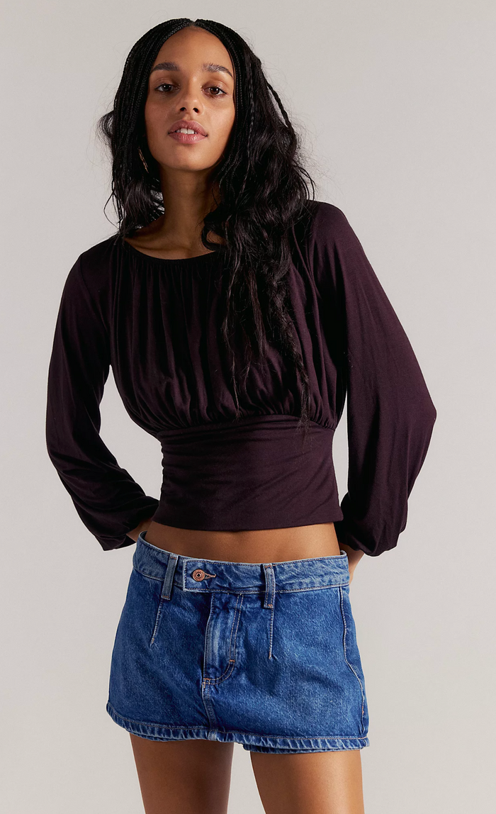 Woman wearing a dark purple top and denim skorts on a plain background