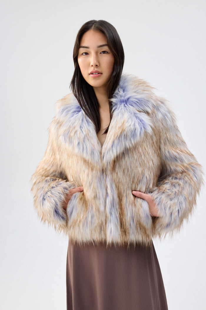 Close-up of a model wearing a cream and blue faux fur jacket with notch lapel and oversized collar, hands in pockets