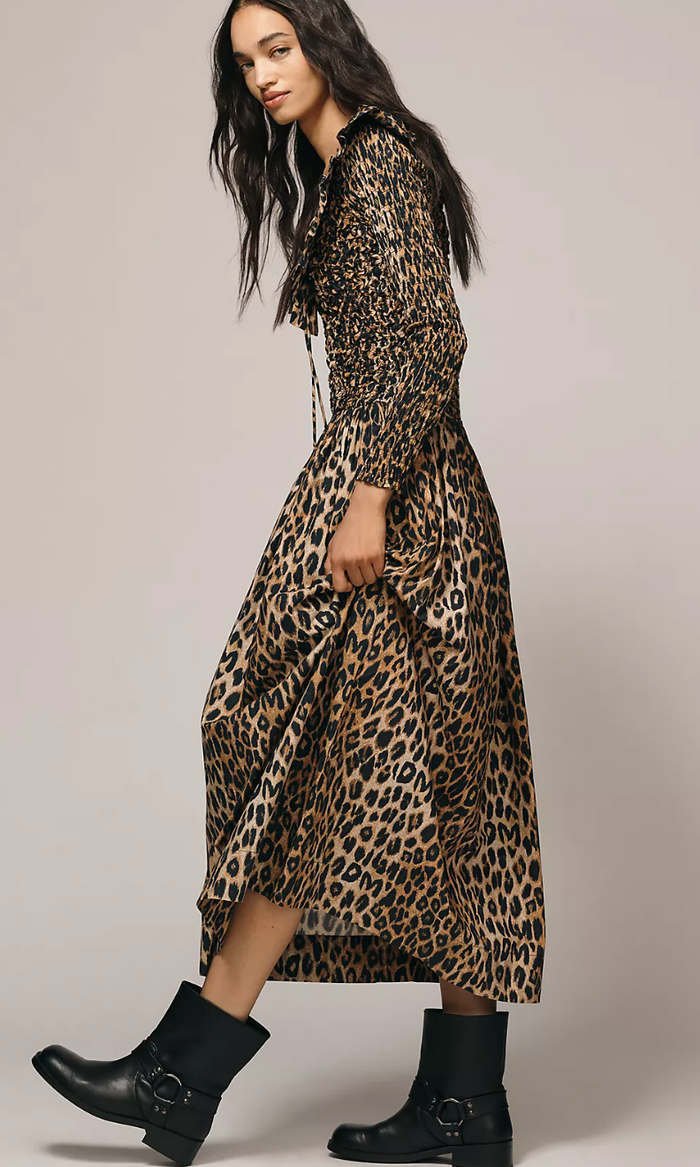 Woman wearing a leopard print dress with black boots on a plain background