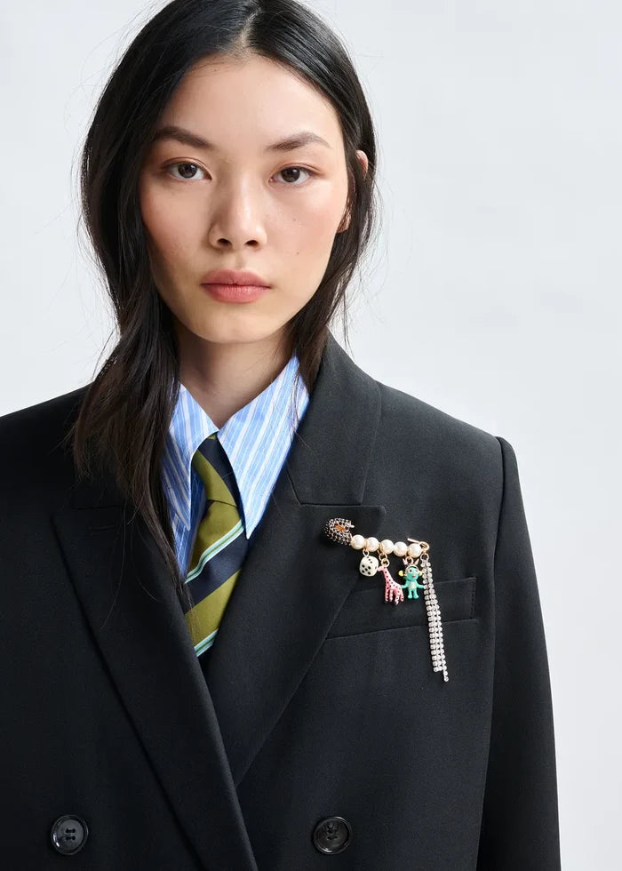 Person wearing a dark suit with a colorful brooch on a light gray background