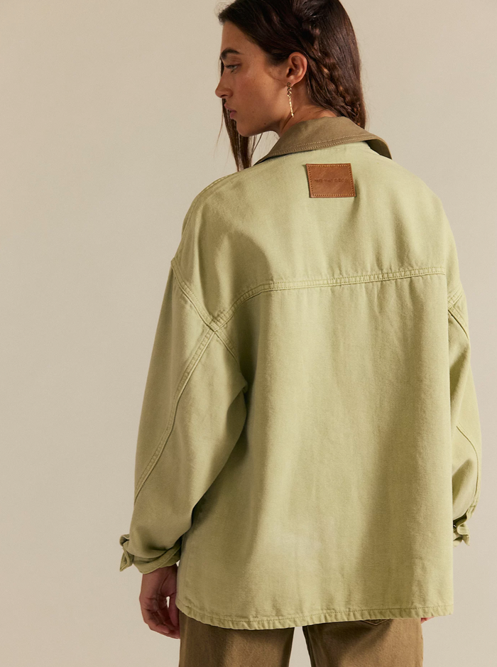 Person wearing a washed sage jacket with a brand patch on a beige background