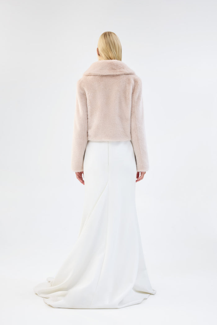 Back view of a blush pink faux fur jacket with notch lapel and cropped fit, worn over a white bridal dress