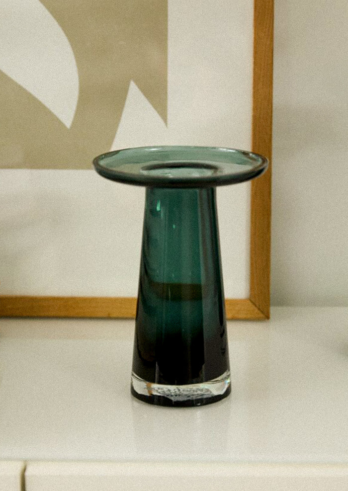 A glass vase in dark teal color, with round, saucer-like top.