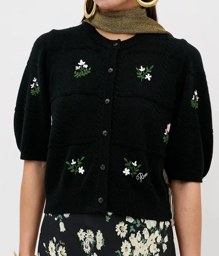 A black knit cardigan with puff sleeves and embroidered white and pink flowers with green leaves, featuring a button-down front and a visible 'Pier St. Cloud' logo on the lower right pocket.