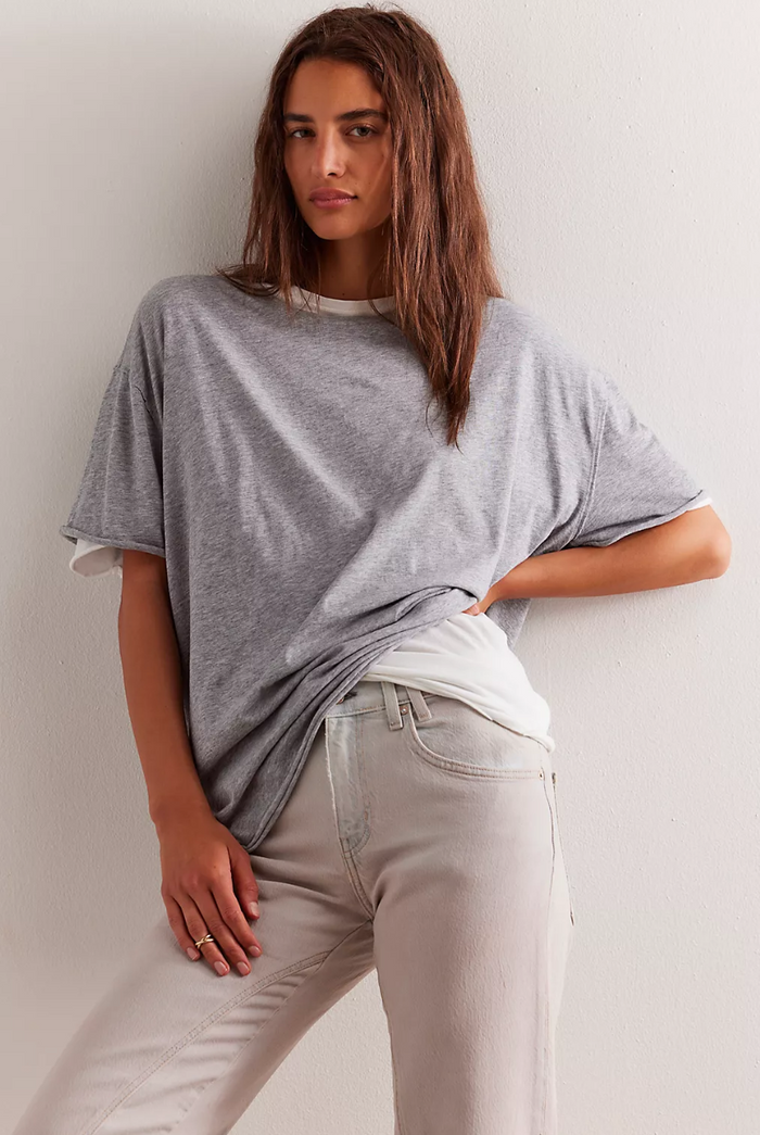 Woman wearing a gray oversized t-shirt and light-colored pants against a plain background