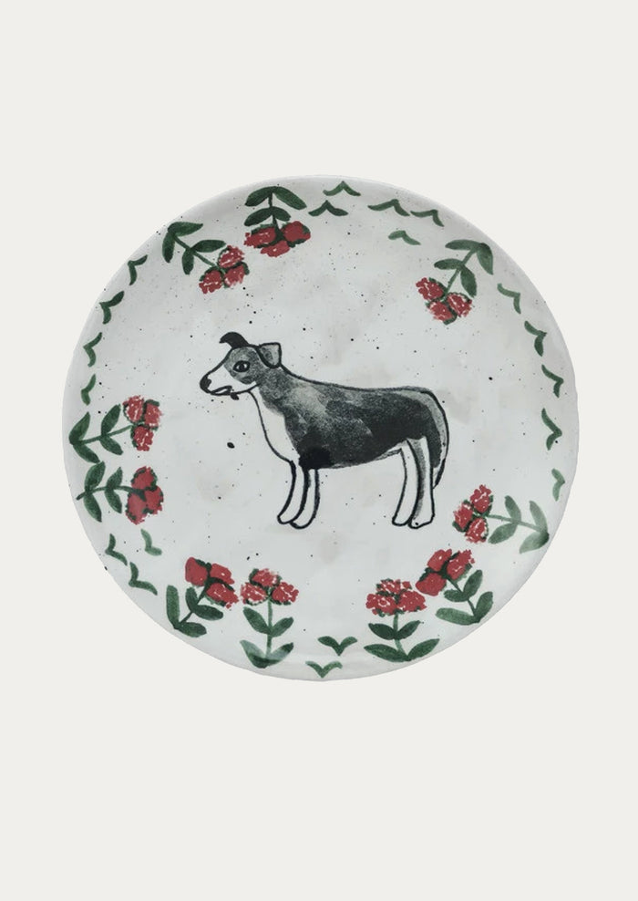 A small ceramic plate with hand painted imagery of black and white dog with red flowers.