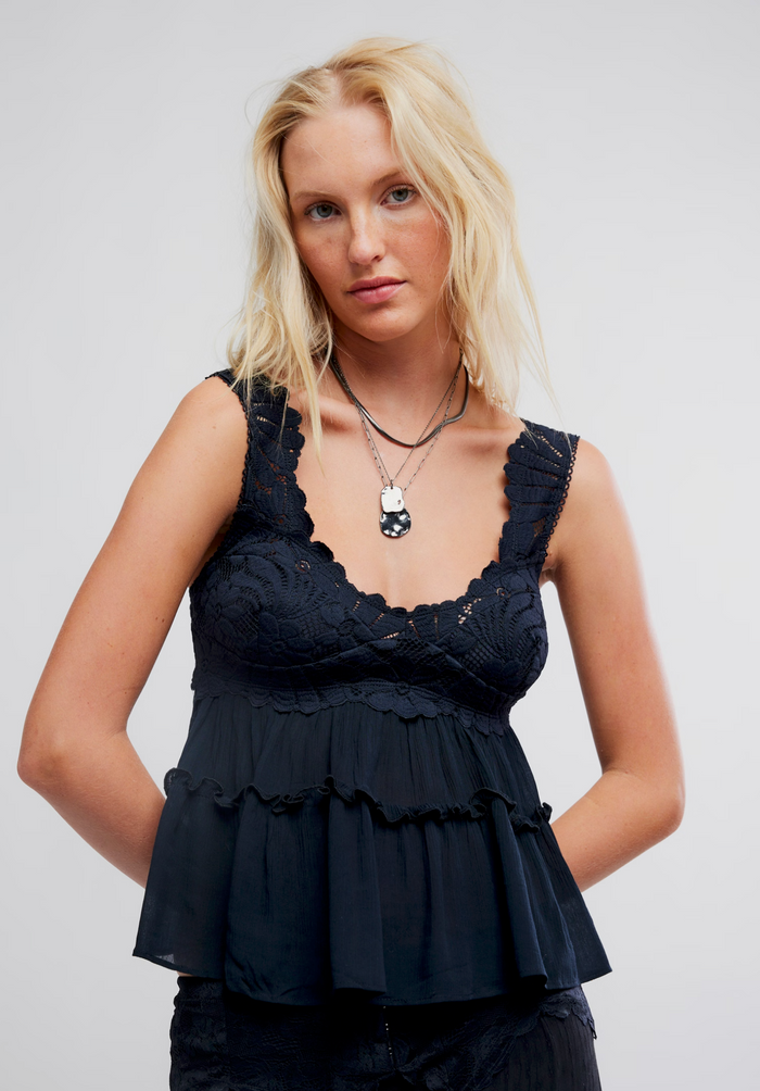 A blonde woman modeling a black lace and ruffle sleeveless top against a light gray studio background.