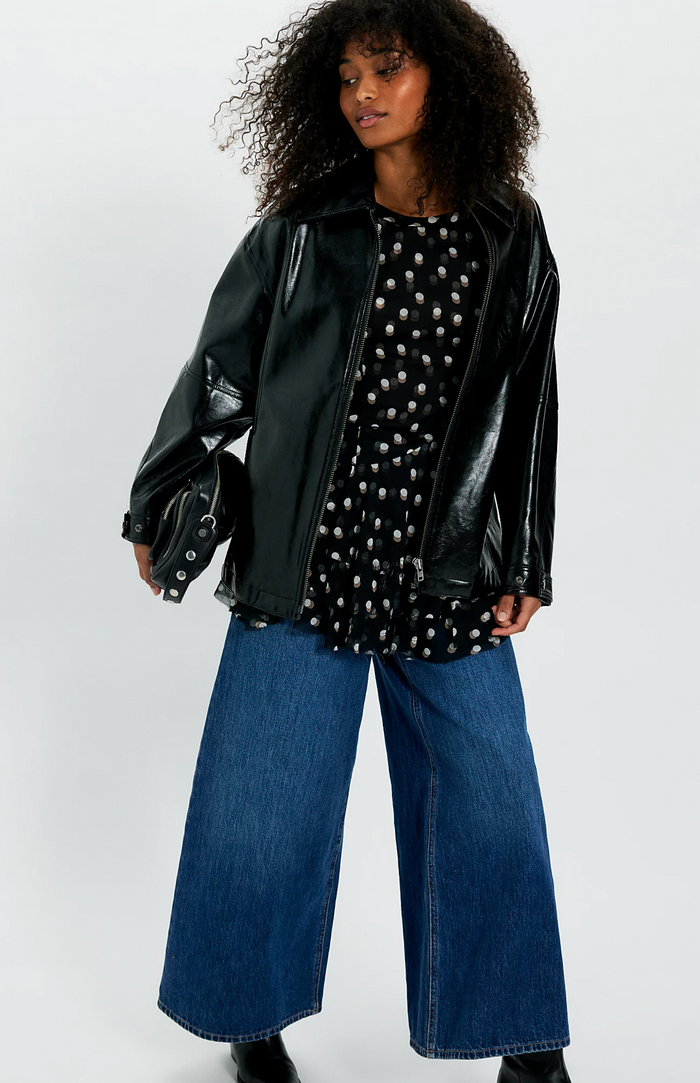Person wearing a black leather jacket, polka dot top, and blue jeans on a white background