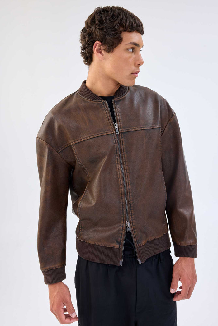 Side profile of a model wearing a brown faux leather jacket with band collar and zip-front closure, worn over black trousers