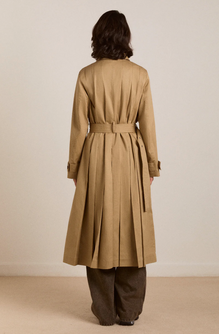 Person wearing a beige trench coat against a plain background