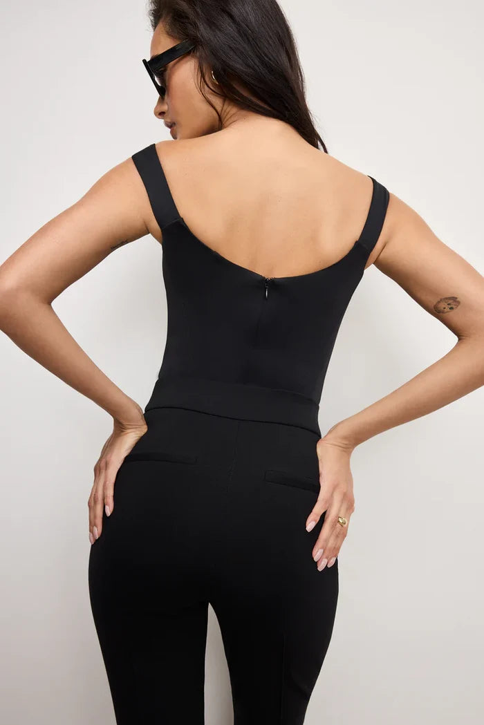 Woman wearing a black sleeveless top and black pants against a plain background