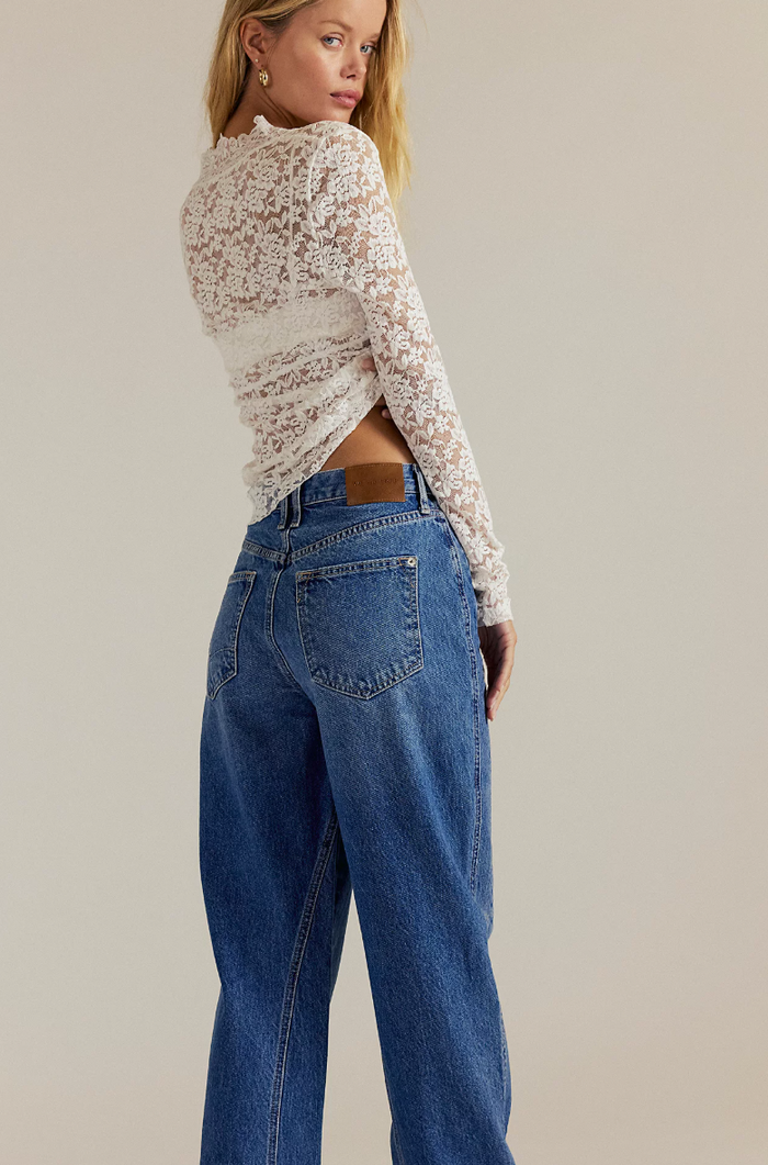 Woman wearing a floral long-sleeve top and blue jeans against a neutral background