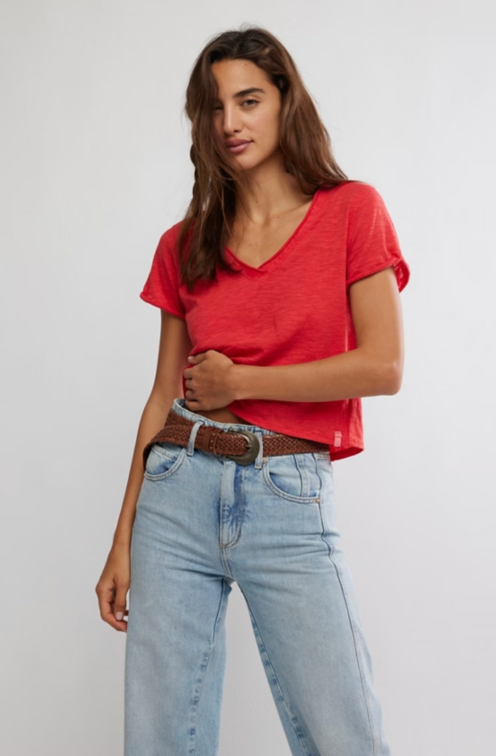 Woman wearing a red t-shirt and light blue jeans against a plain background