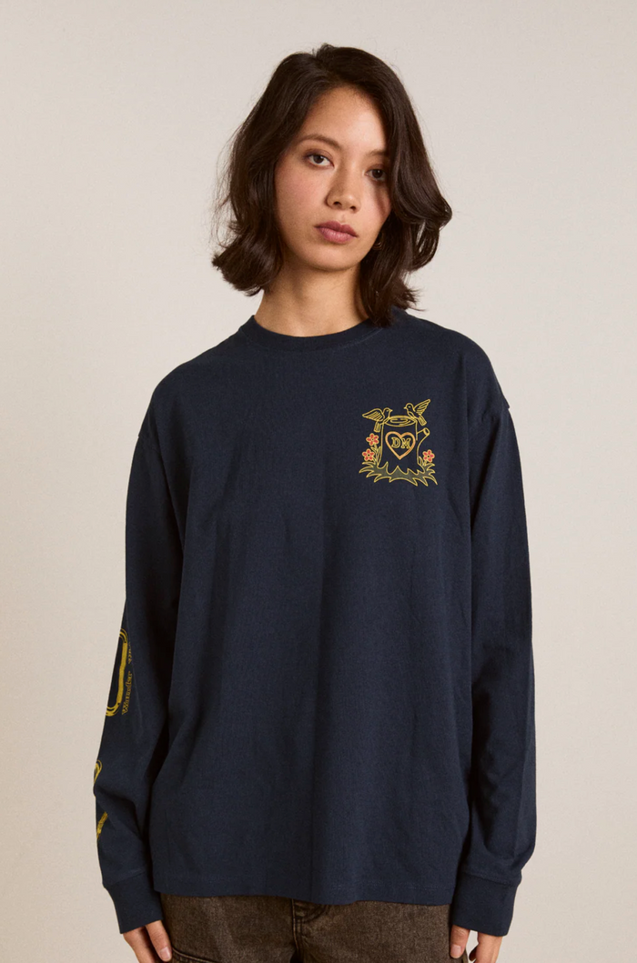 Person wearing a navy blue long-sleeve shirt with a gold emblem on a beige background