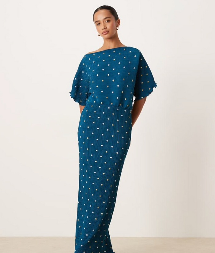Woman wearing a blue dress with white polka dots on a plain background