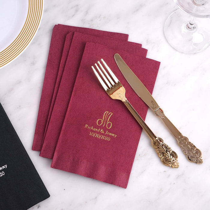 Personalized burgundy napkins with gold foil, fork, and knife on marble table.