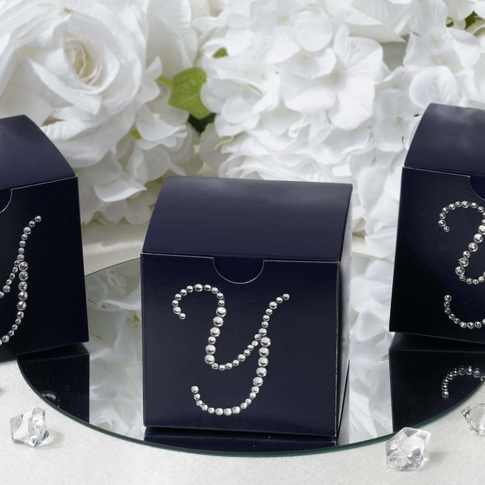 Navy gift boxes with rhinestone 'Y' on a mirrored surface surrounded by flowers. #whtbkgd