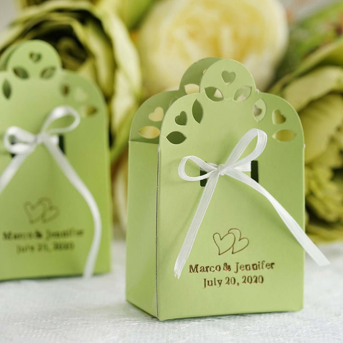 Personalized green wedding favor boxes with heart cutouts and white ribbon.