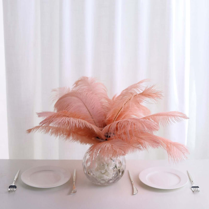 Pink feather centerpiece in a glass vase on a dining table with white plates.