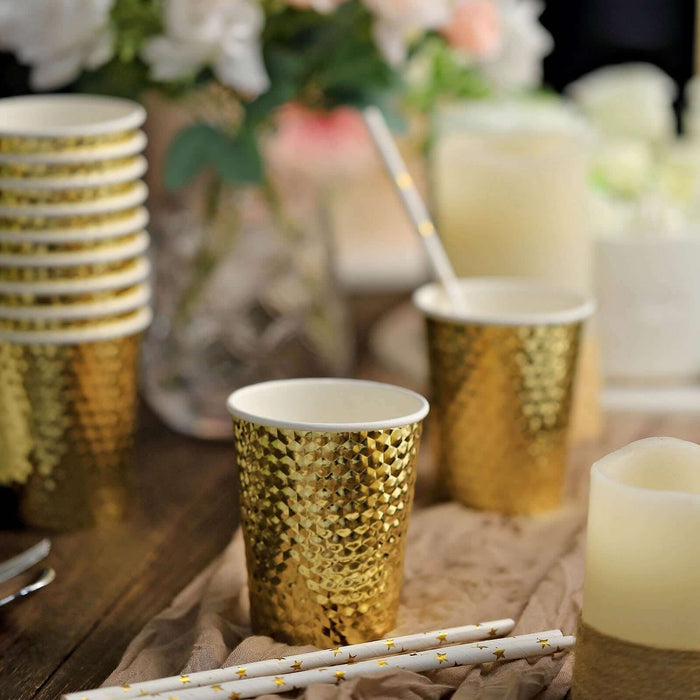 Gold textured party cups with gold straws on a rustic table setting.