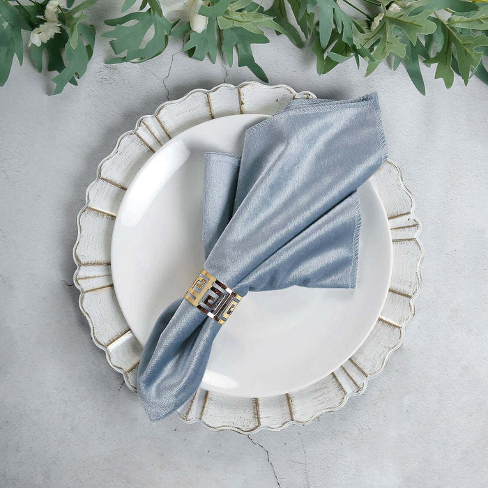 Elegant blue napkin with decorative ring on a white plate, styled with greenery.
