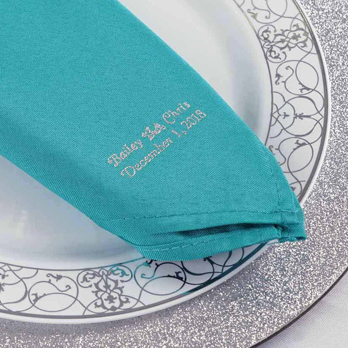 Embroidered teal napkin on a decorative plate for special occasions. #whtbkgd