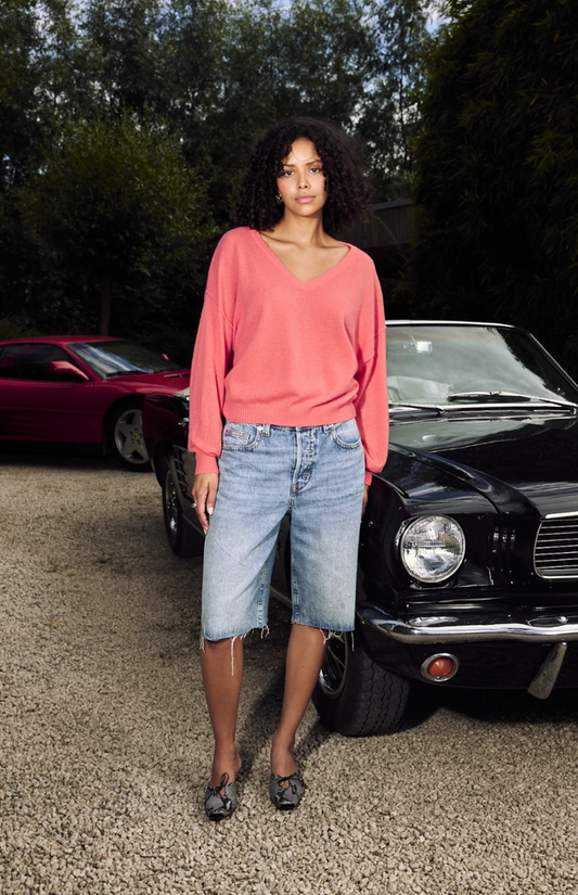 Woman in a cerise sweater and denim skirt standing in front of vintage cars.
