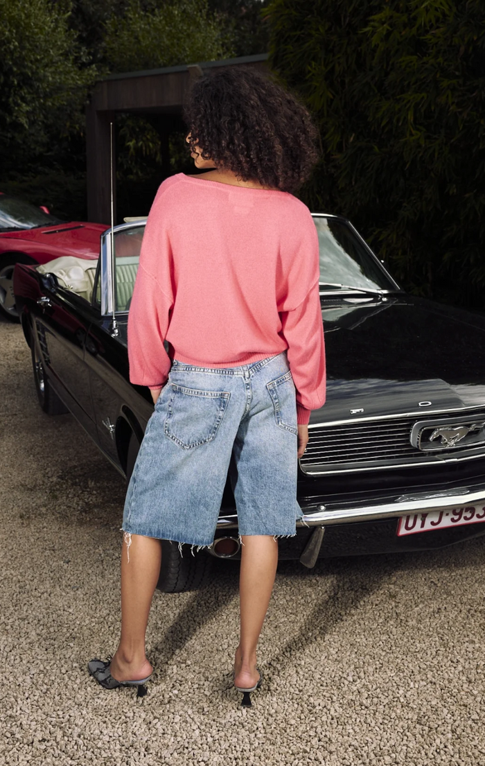 Woman standing next to a vintage car wearing a cerise sweater and denim skirt.