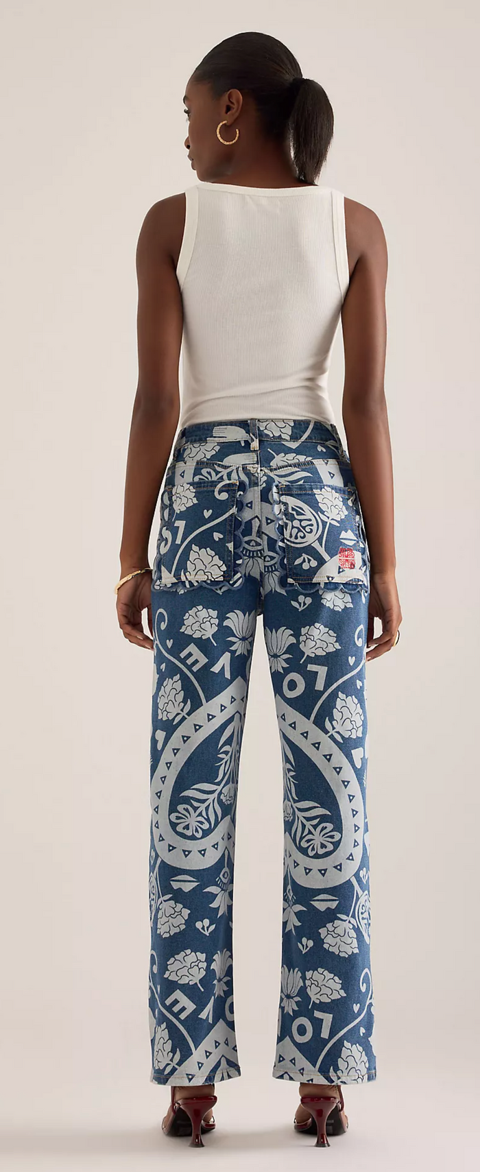Woman wearing a white sleeveless top and blue patterned pants on a plain background