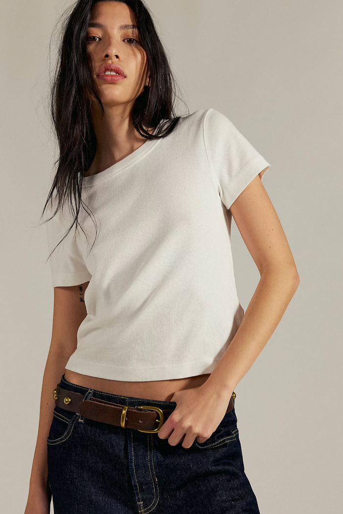 Woman wearing a Free People ivory t-shirt and dark jeans against a neutral background
