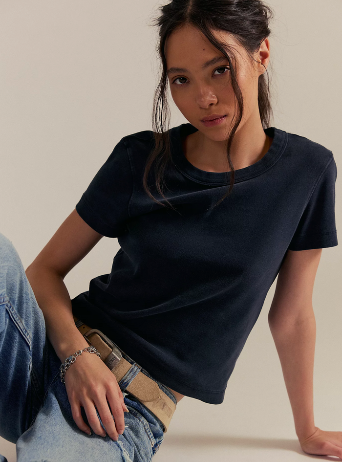 Woman wearing a black Free People t-shirt and blue jeans sitting on a beige background