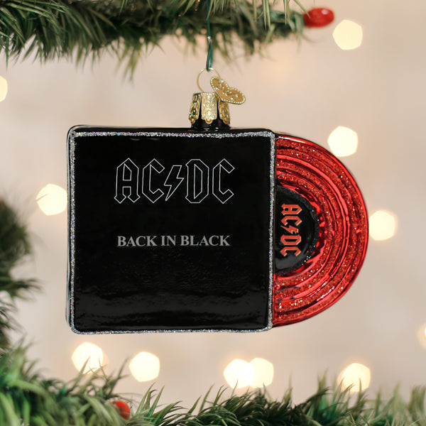 A Christmas tree ornament shaped like a vinyl record and album cover for AC/DCs Back in Black hangs from a branch, with festive lights blurred in the background.