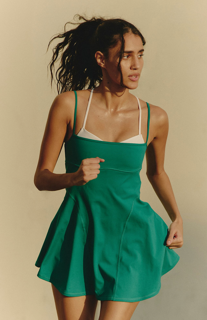 Woman wearing a green dress with a white top against a beige background