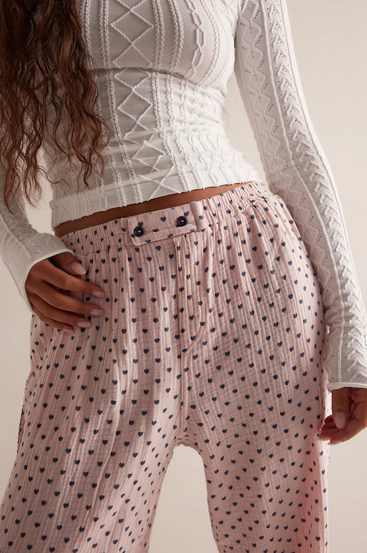 Person wearing a patterned outfit with a white top and coral heart polka dot be mine pants.