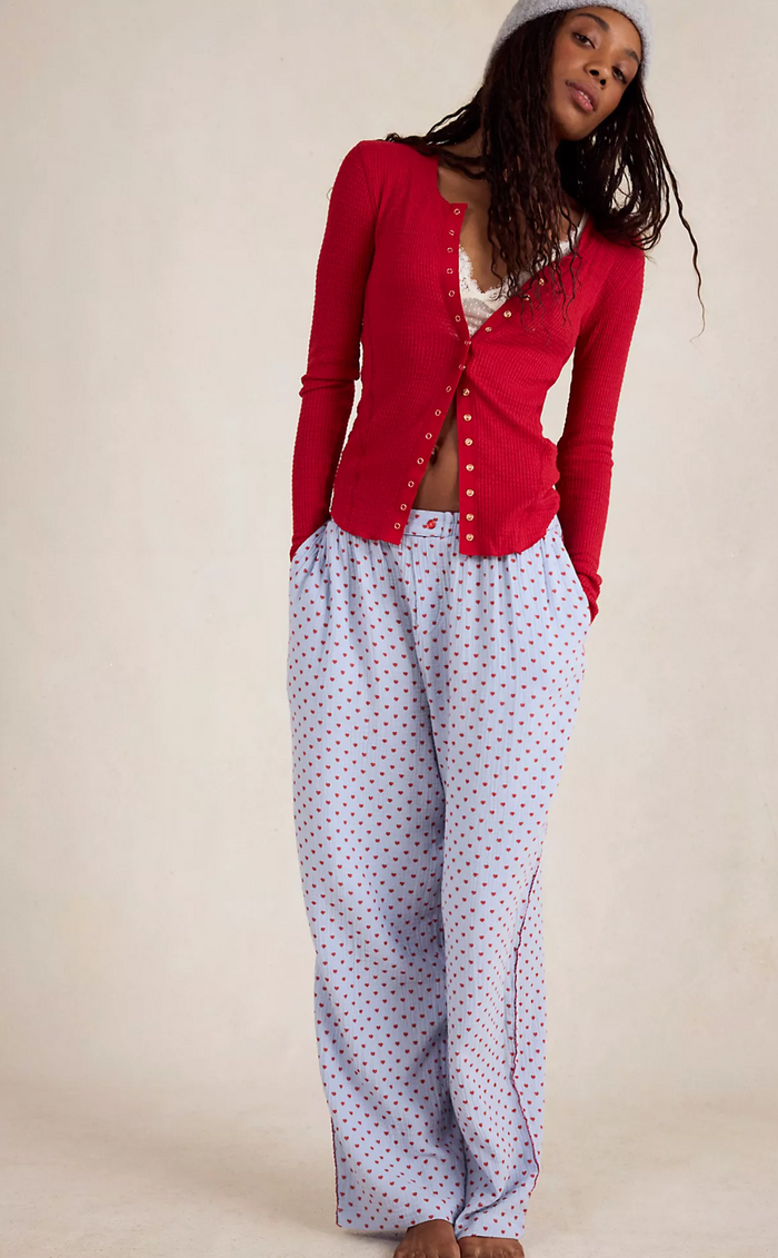 Woman wearing a red cardigan over a white shirt with blue polka dot pants on a beige background