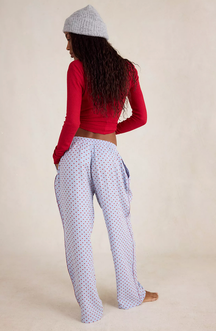 Person wearing a red long-sleeve top and blue pants with hearts on a beige background