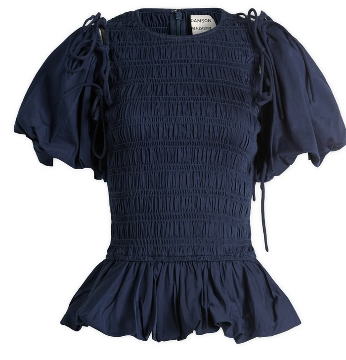 A navy blue smocked blouse with puff sleeves, tie details at the shoulders, and a ruffled hem, shown against a plain white background.