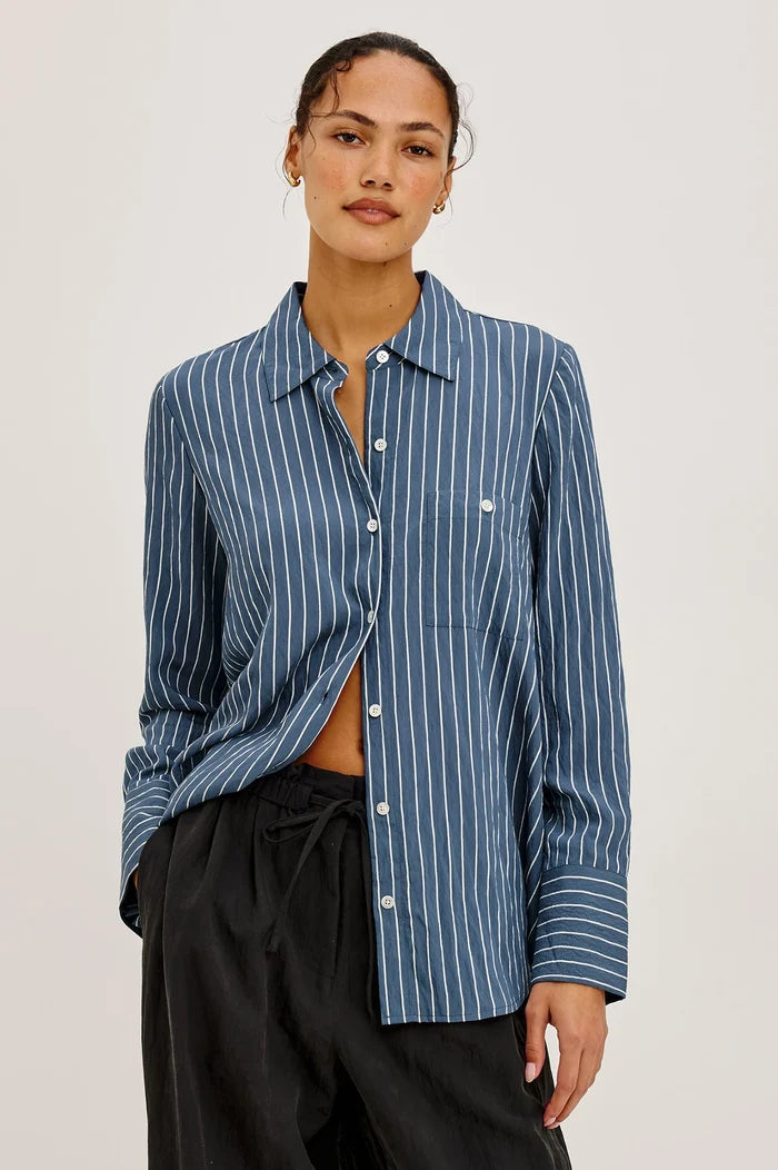 Woman wearing a blue striped shirt and black trousers with a white background