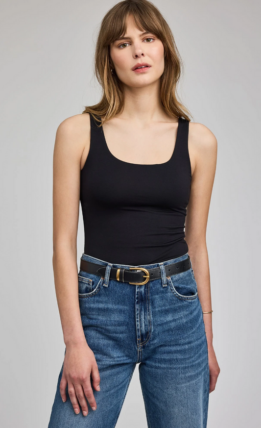 Woman wearing a black tank top and blue jeans on a gray background