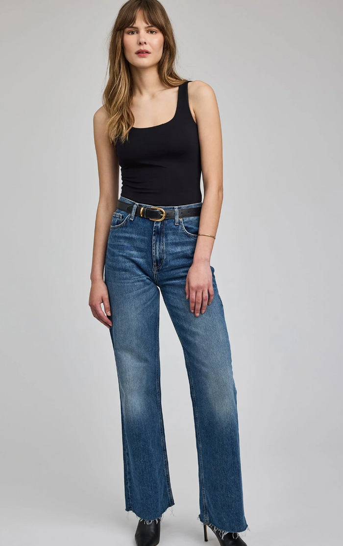 Woman wearing a black tank top and blue jeans on a gray background
