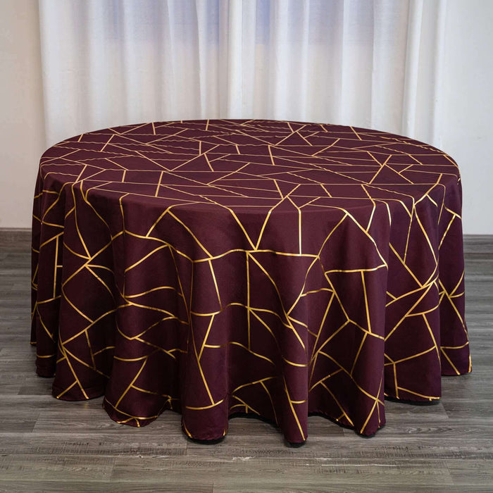 Round burgundy tablecloth with gold geometric pattern on a wooden surface.