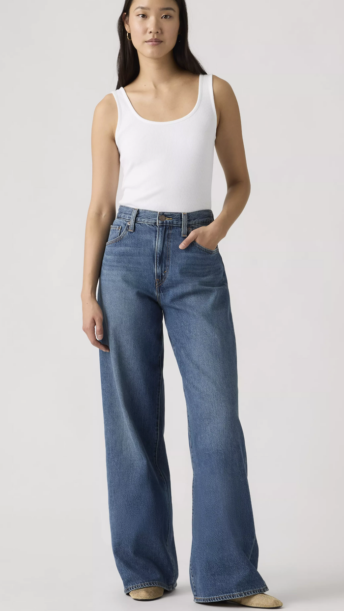 Woman wearing a white tank top and blue jeans on a plain background