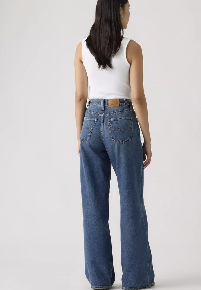 Person wearing blue jeans and a white tank top on a plain background